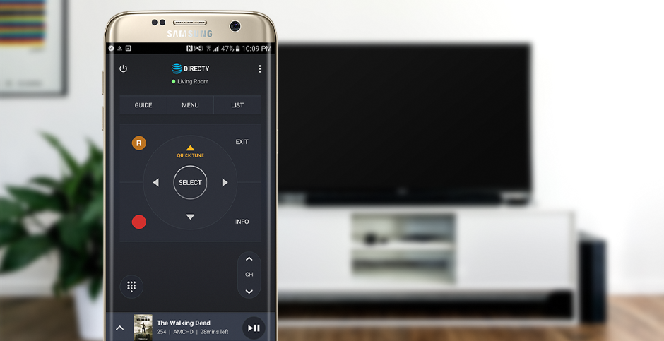 DIRECTV Remote app shown on an Android phone with a full-size TV in the background. The app allows users to control their DIRECTV receivers from their phones.
